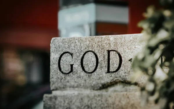 The word GOD carved into a stone monument, with soft-focus greenery beside it