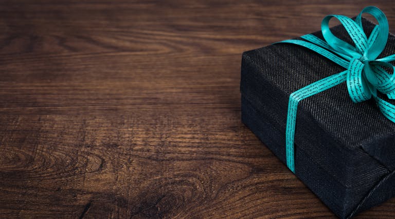 A stylish black gift box with blue ribbon on a wooden table, perfect for celebrations.